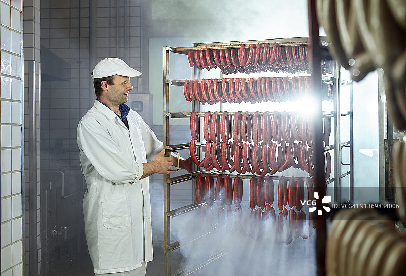 微笑的屠夫看着烟熏房里排列好的香肠图片素材