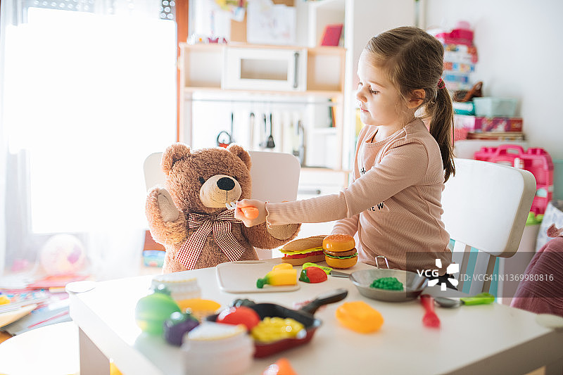 小女孩们在家玩玩具，喂泰迪熊图片素材