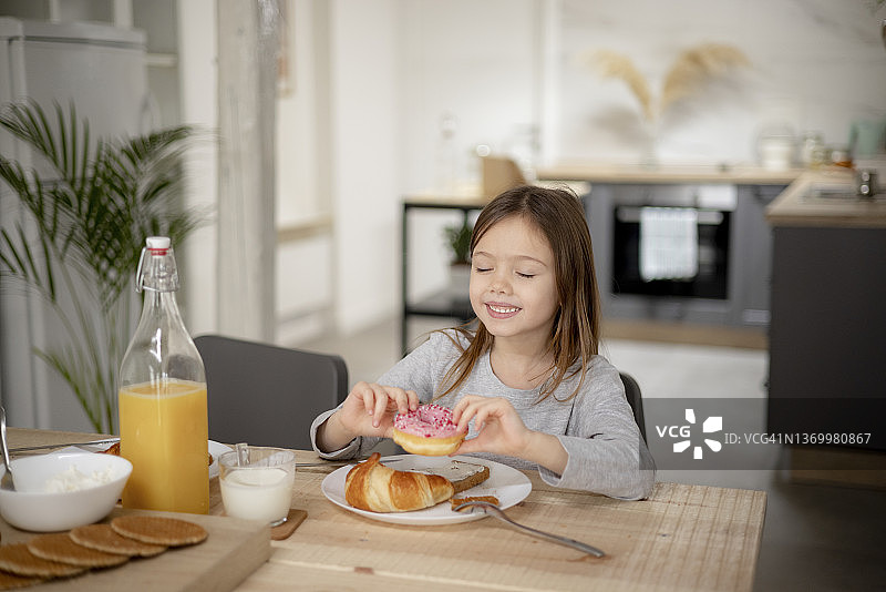 快乐的高加索小女孩在家享用美味的甜甜圈图片素材