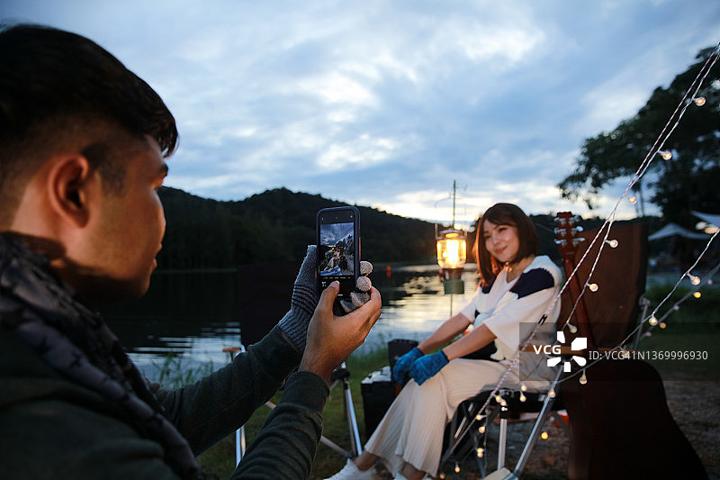 男子在森林湖边的露营帐篷前用手机拍摄女友，户外探险旅行图片素材