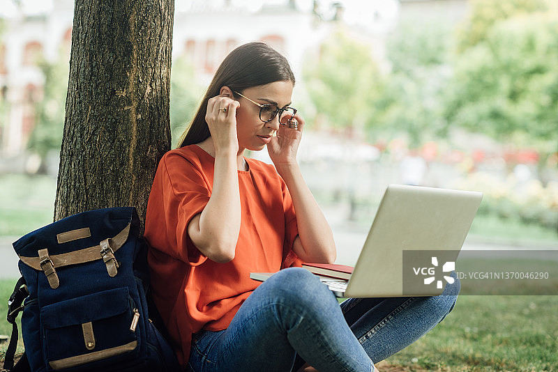 女孩坐在公园草地上网课学习图片素材