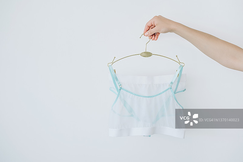 白色墙壁上手持金属衣架和浅色内衣的女人图片素材