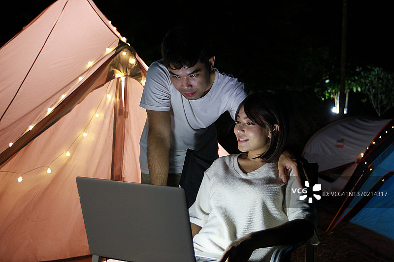 年轻情侣在森林露营帐篷里远程工作，夏季探险度假概念图片素材