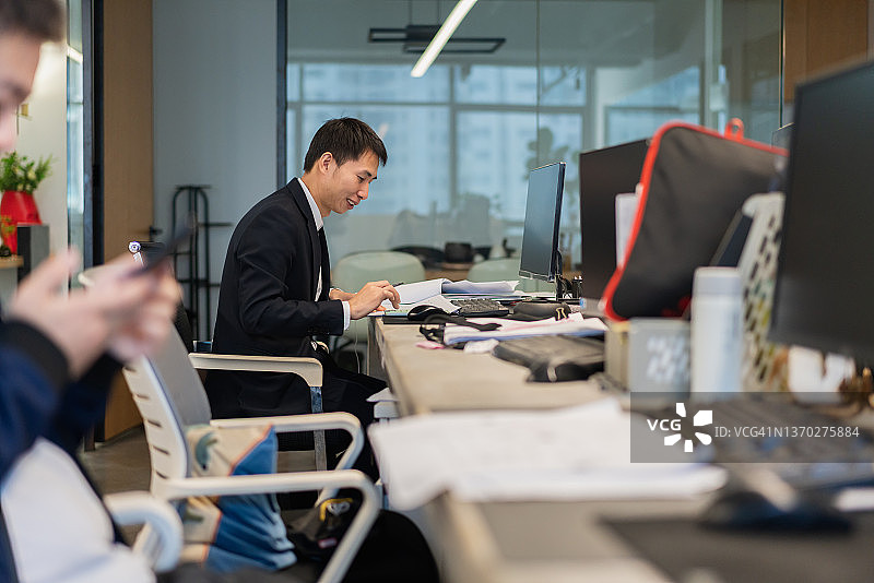 在办公室工作站努力工作，使用计算器进行计算的男人图片素材