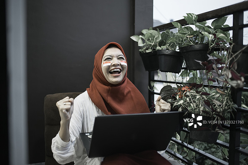 年轻漂亮的印尼妇女戴着头巾，支持印尼国家队，在线观看，挥舞印尼国旗，庆祝印尼独立日图片素材