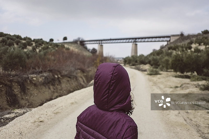 在阴天独自走向旧桥结构的戴帽女孩图片素材