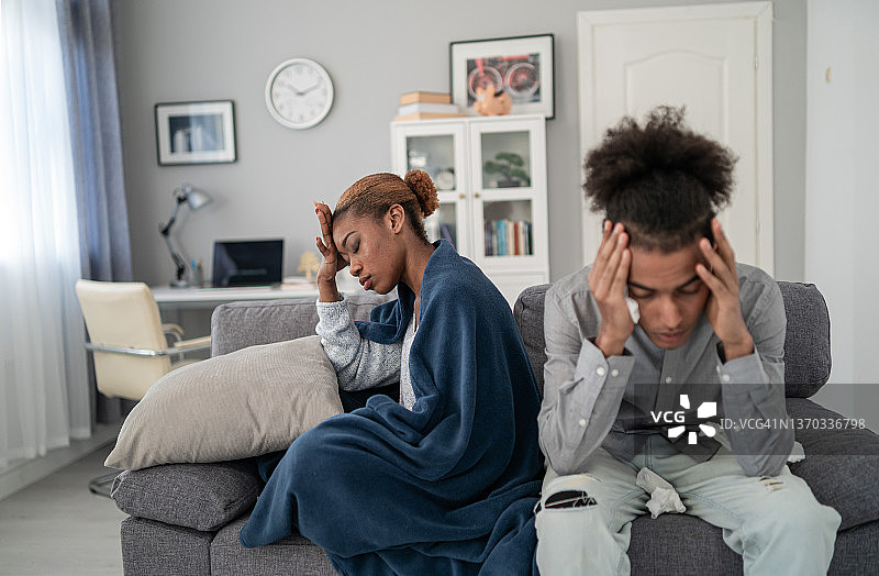生病的年轻非裔美国夫妇坐在家里的沙发上，两人都在擤鼻涕，女人身上盖着毯子图片素材