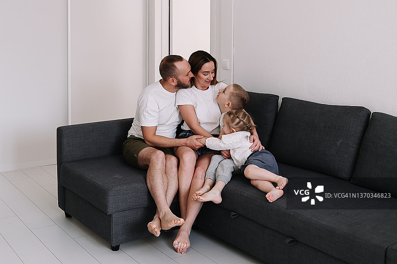 幸福的一家四口在周末的家里共度时光。妈妈、爸爸和孩子们在休息日放松地依偎在沙发上。家庭生活图片素材