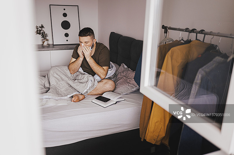 年轻男人坐在床上，患有流感图片素材