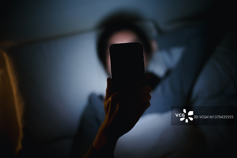 年轻的亚洲女人在舒适卧室的床上用智能手机上网图片素材