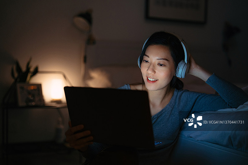 在舒适的卧室里深夜用笔记本电脑看电影的放松的亚洲年轻女人图片素材