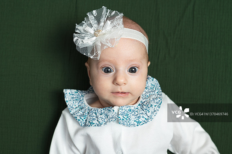 一个头上缠着绷带、身穿白色婴儿连体衣的女婴的肖像图片素材