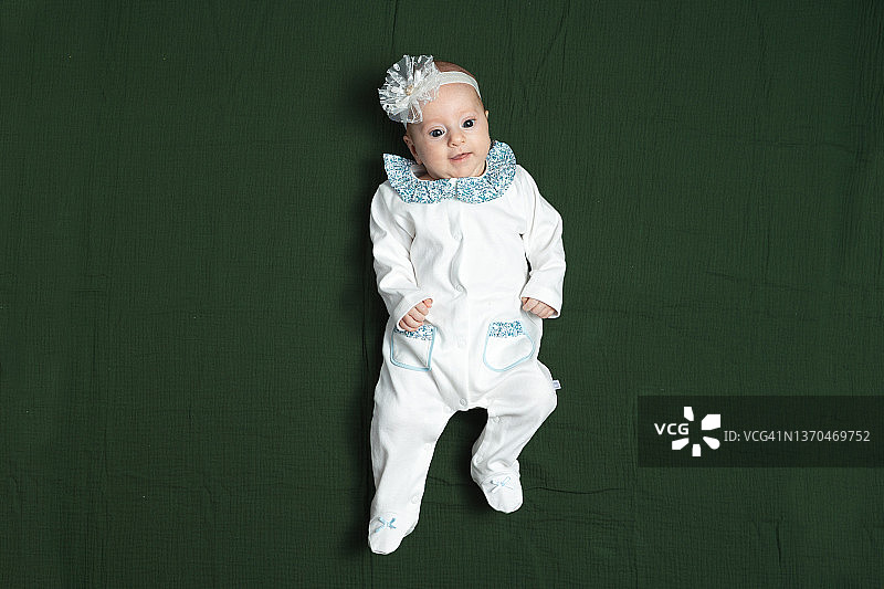 一个头上缠着绷带、身穿白色婴儿连体衣的女婴的肖像图片素材