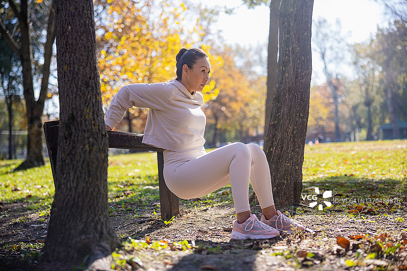 在公园里穿着休闲运动服靠在木栅栏上做屈臂撑的亚洲女人图片素材