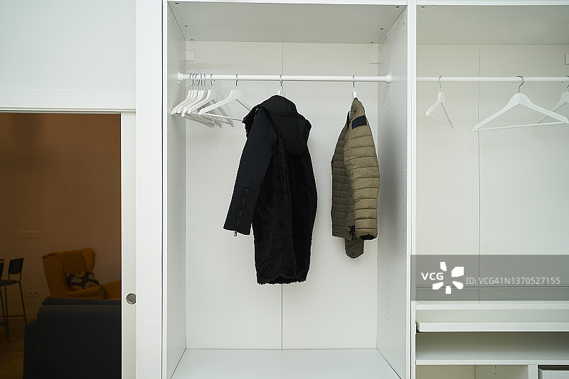 特写：白色衣柜，两个外套挂在衣架上，旁边是几个空的白色衣架图片素材