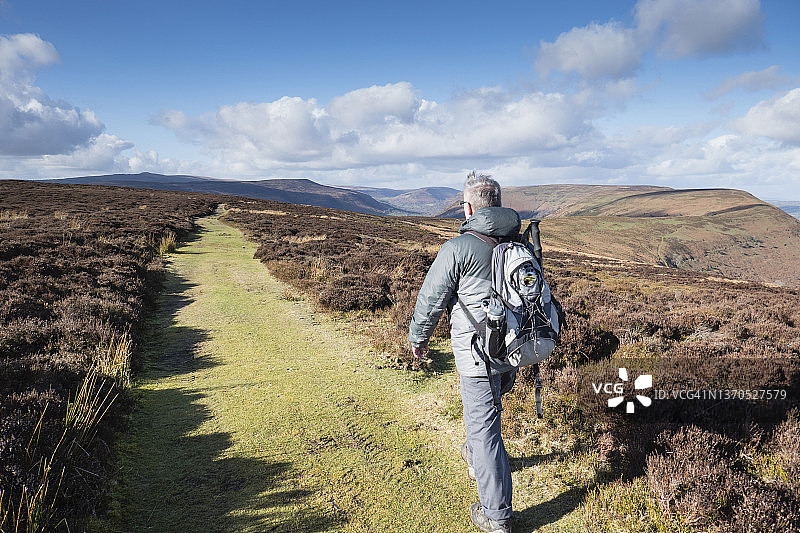 年长的白人男子在蒙茅斯郡的步行道上背着背包；图片拍摄于英国威尔士蒙茅斯郡的蒙茅斯郡路和奥法堤路，二月图片素材