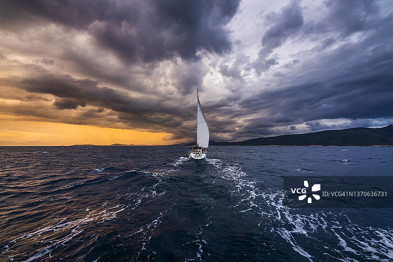 暴风雨日落云海上的白色风帆游艇图片素材