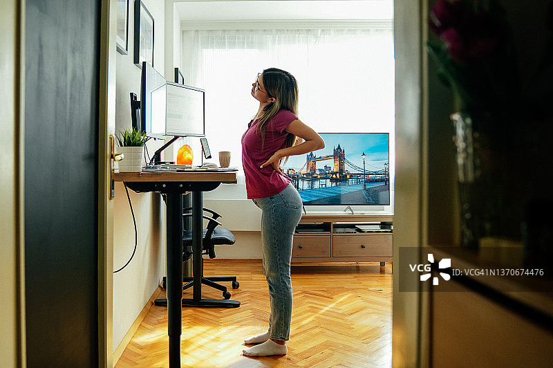 在家里的站立式办公桌前工作，背痛的女人图片素材