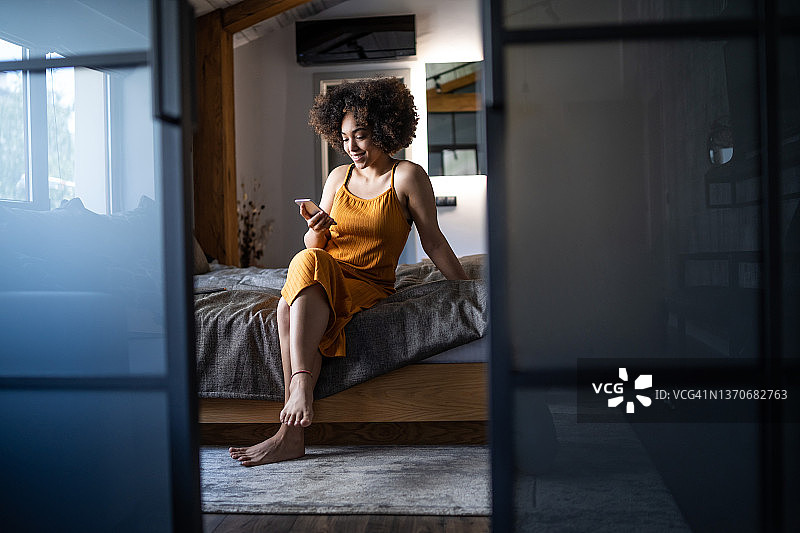美丽的非洲裔女人们坐在床上使用智能手机图片素材