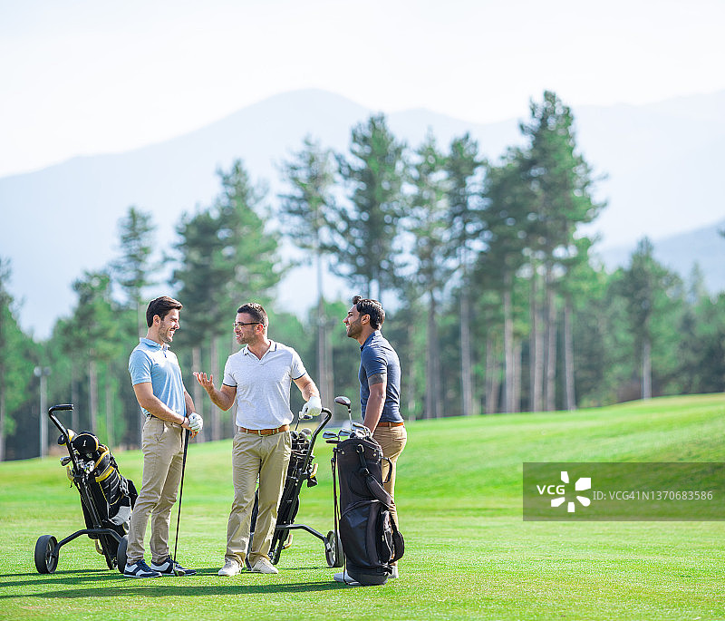 一群男性高尔夫球友在阳光明媚的日子里打高尔夫，在球场上交谈微笑图片素材