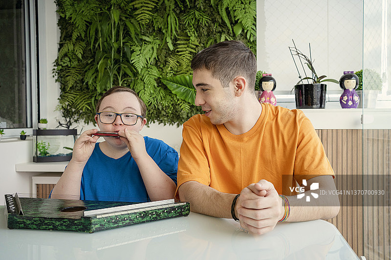 患有唐氏综合症的男孩和他的兄弟学习音乐。弹奏竖琴和口琴图片素材