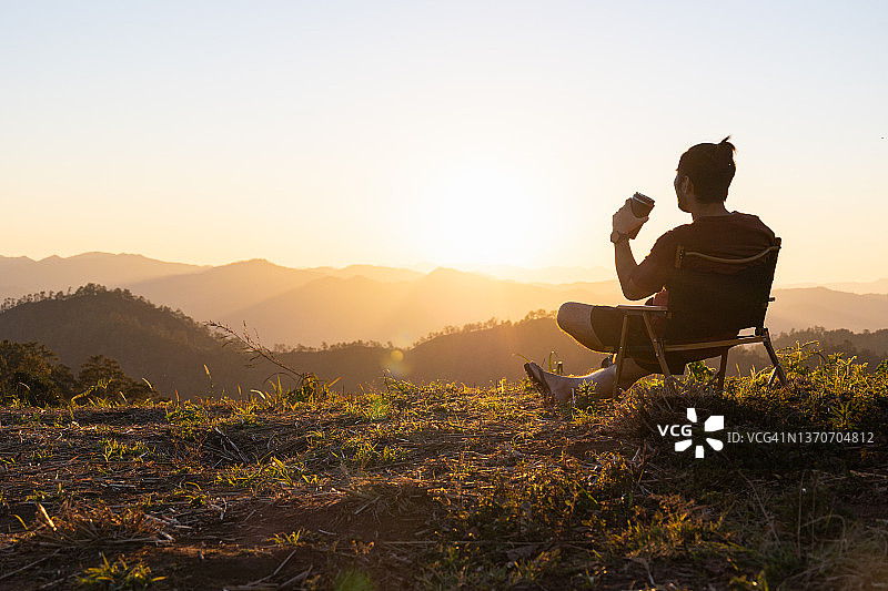 男人坐在山丘上喝咖啡，欣赏美丽的日出和山景，享受平静的生活图片素材