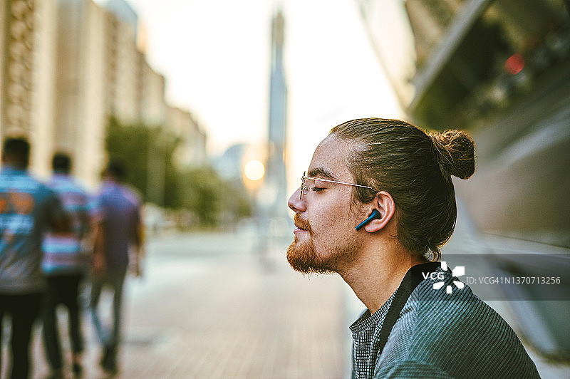 年轻男子独自在城市戴耳机听音乐图片素材