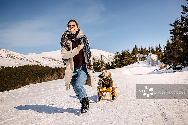 母亲拉着坐在雪橇上的儿子图片素材