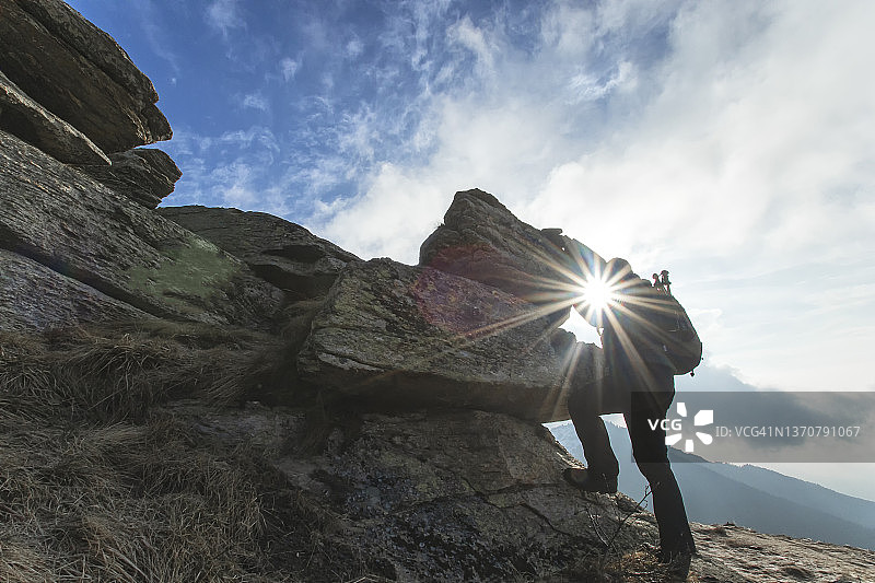 日出时攀登岩石的男性徒步旅行者图片素材