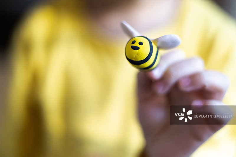 穿着亮黄色衬衫拿着可爱黏土蜜蜂的混血儿童图片素材