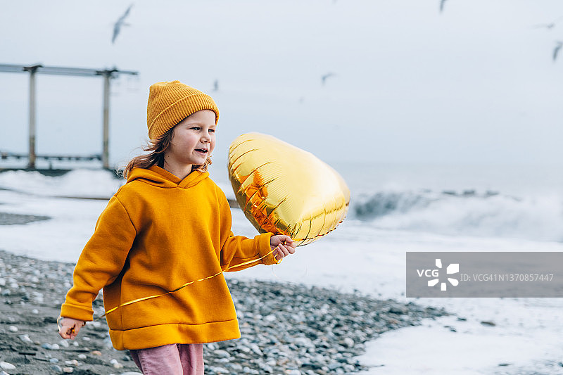 在海滩上拿着黄色心形气球的幼儿图片素材