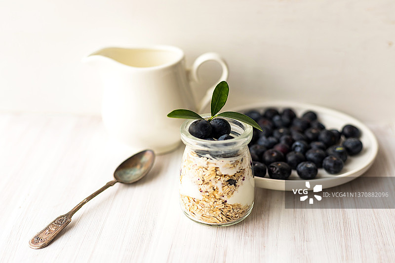 燕麦片格兰诺拉麦片或混合早餐与自制酸奶，新鲜蓝莓和陶瓷壶牛奶白桌图片素材