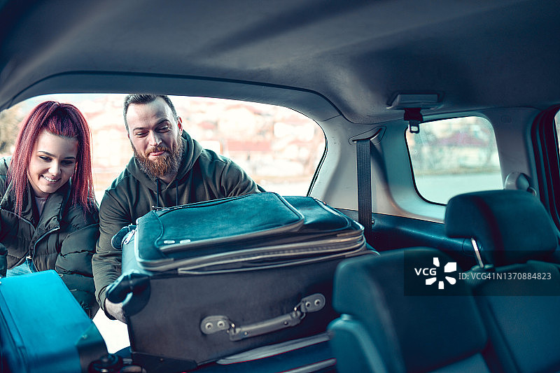 笑着的情侣把包放进汽车后备箱准备旅行图片素材