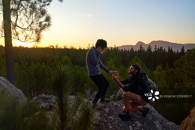 日落时分，戴着订婚戒指的年轻男子在岩石上向女子求婚图片素材