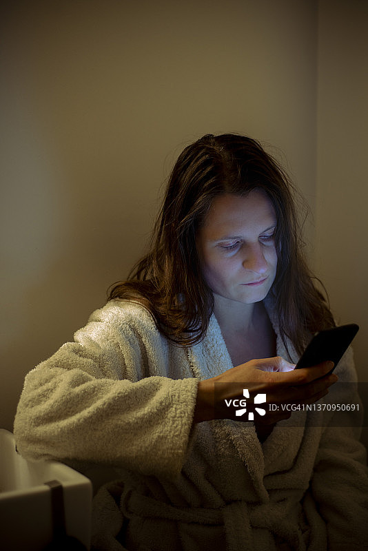 在浴室里玩手机的孤独中年妇女图片素材