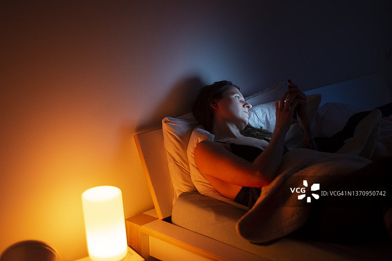 在床上玩手机的孤独中年女人图片素材