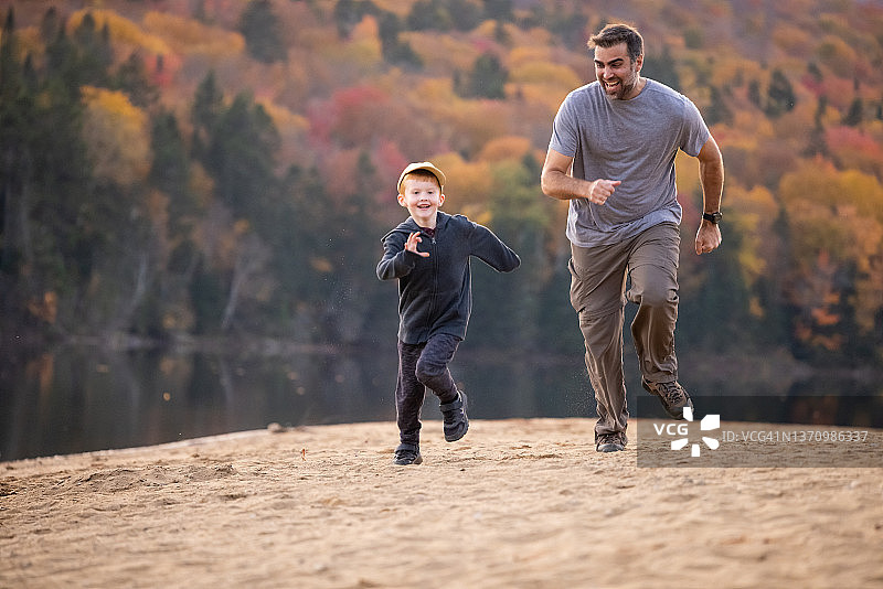 可爱的红发男孩和父亲在加拿大魁北克省翠湖山国家公园的秋季海滩上奔跑图片素材