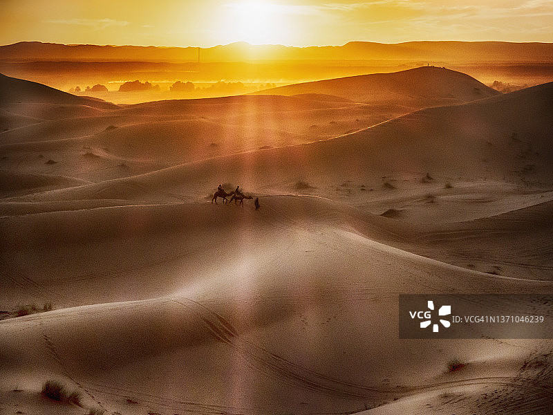 日落时分，在摩洛哥撒哈拉沙漠中牵着两匹骆驼的男人剪影图片素材