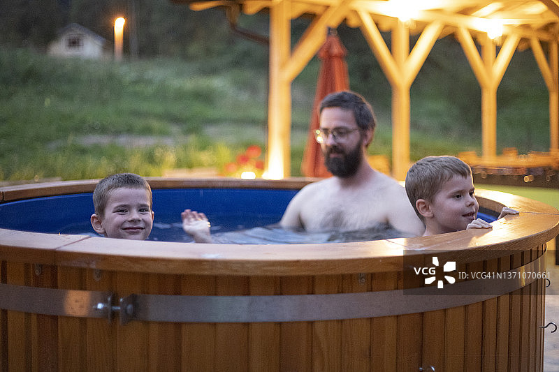 两个男孩和爸爸在山间度假村的温泉浴缸中享受夜晚图片素材