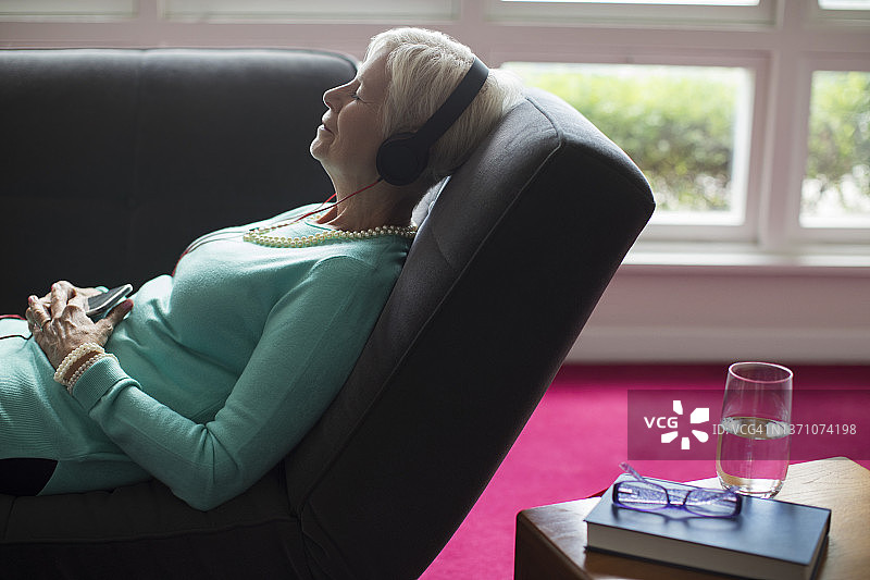沙发上戴耳机听音乐的年长女人图片素材