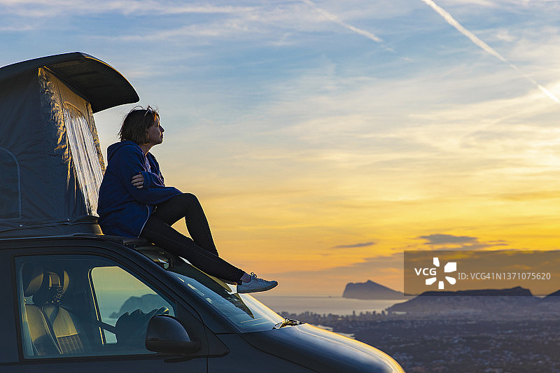 中年妇女在露营车顶欣赏日落美景图片素材