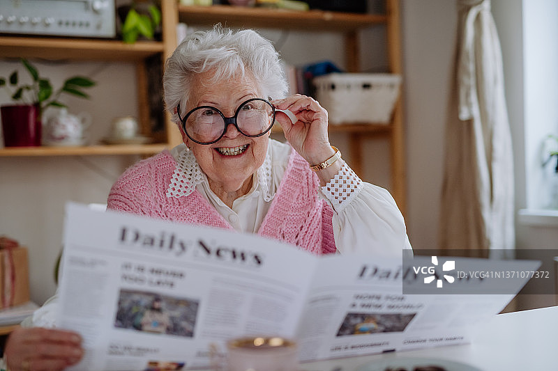 戴着滑稽眼镜在家看报纸并看向镜头的年长女性图片素材