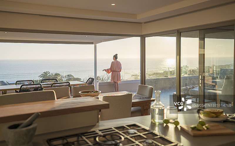 在阳光明媚的豪华阳台上，穿着浴袍放松身心，欣赏海景的女人图片素材