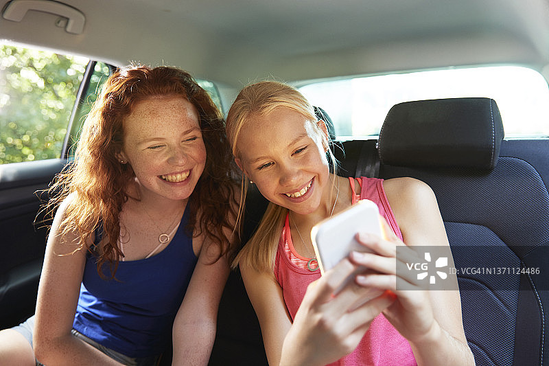 快乐的青少年女孩朋友在汽车后座自拍图片素材