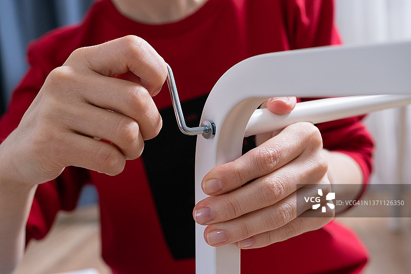 年轻女子坐在地板上按照说明组装家具，修理椅子，改善室内装饰。女性用螺丝刀拧紧螺钉或固定螺栓，在家快速组装家具。图片素材