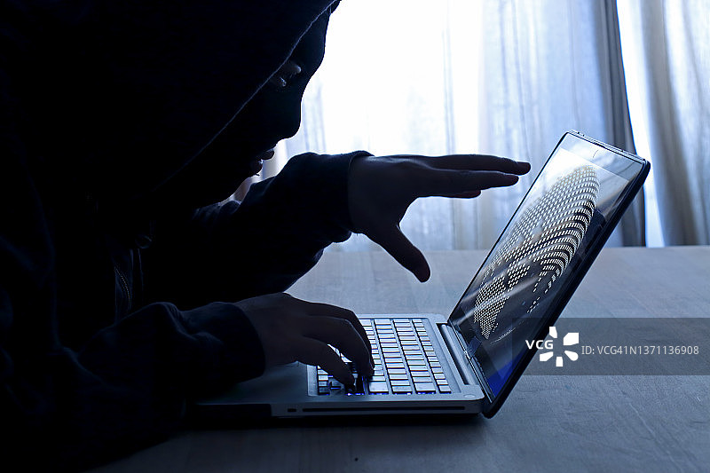电脑程序员或黑客在笔记本电脑键盘上输入代码，试图入侵秘密组织系统。互联网犯罪概念图片素材
