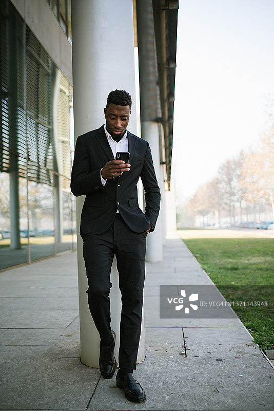 放松的黑人男商人在柱子附近使用手机图片素材