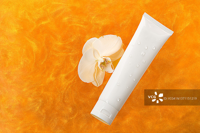 白色软管面霜或护手霜和橙色液体质地中的白色兰花图片素材