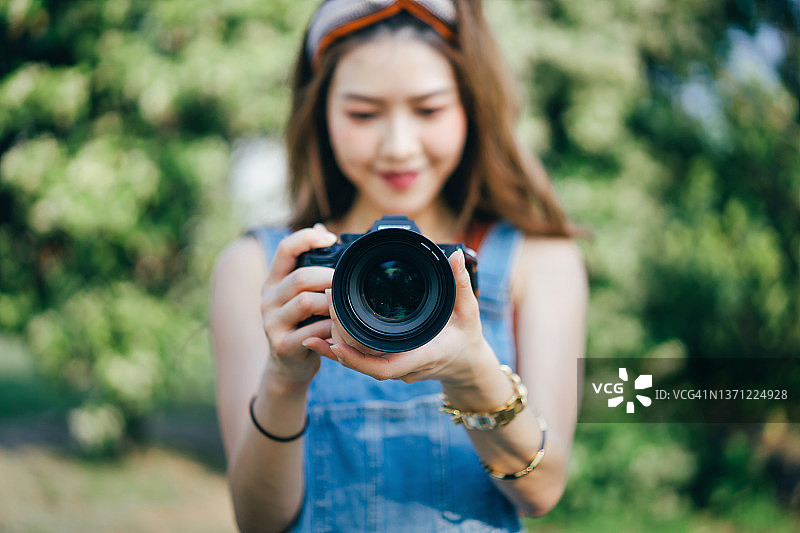 快乐的亚洲女大学生在晴朗的一天在自然公园用相机拍照图片素材