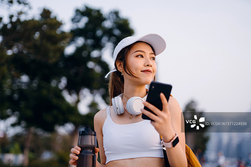 在城市户外锻炼后使用智能手机的亚洲运动女人图片素材